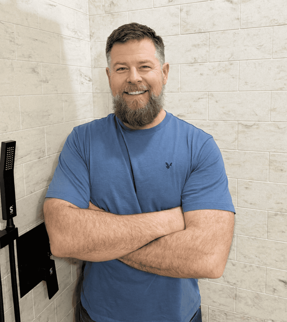 Friendly man with a beard smiling in a bathroom, promoting bathroom renovation services.