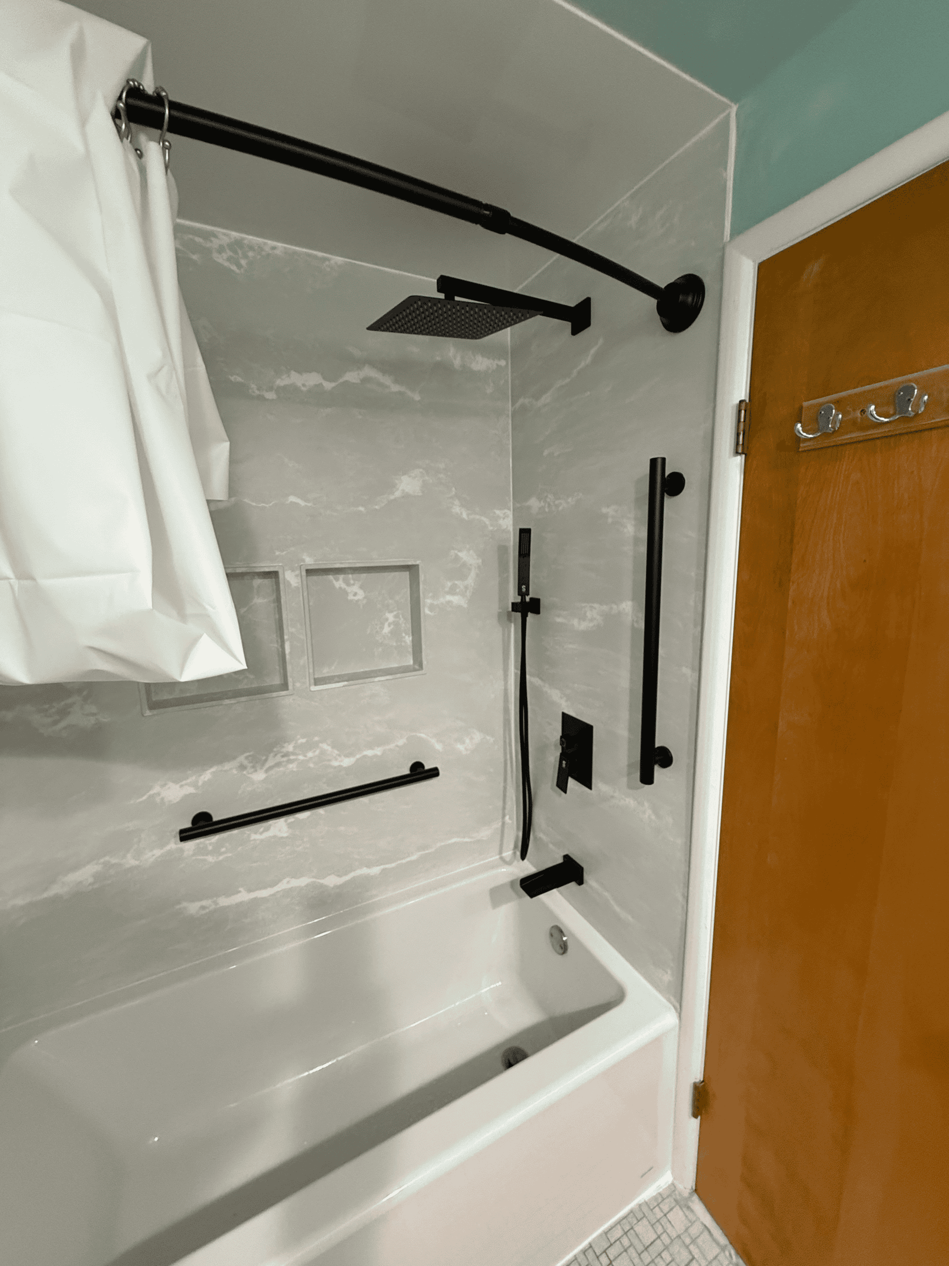 Modern walk-in shower with black fixtures and a bathtub in a bathroom.