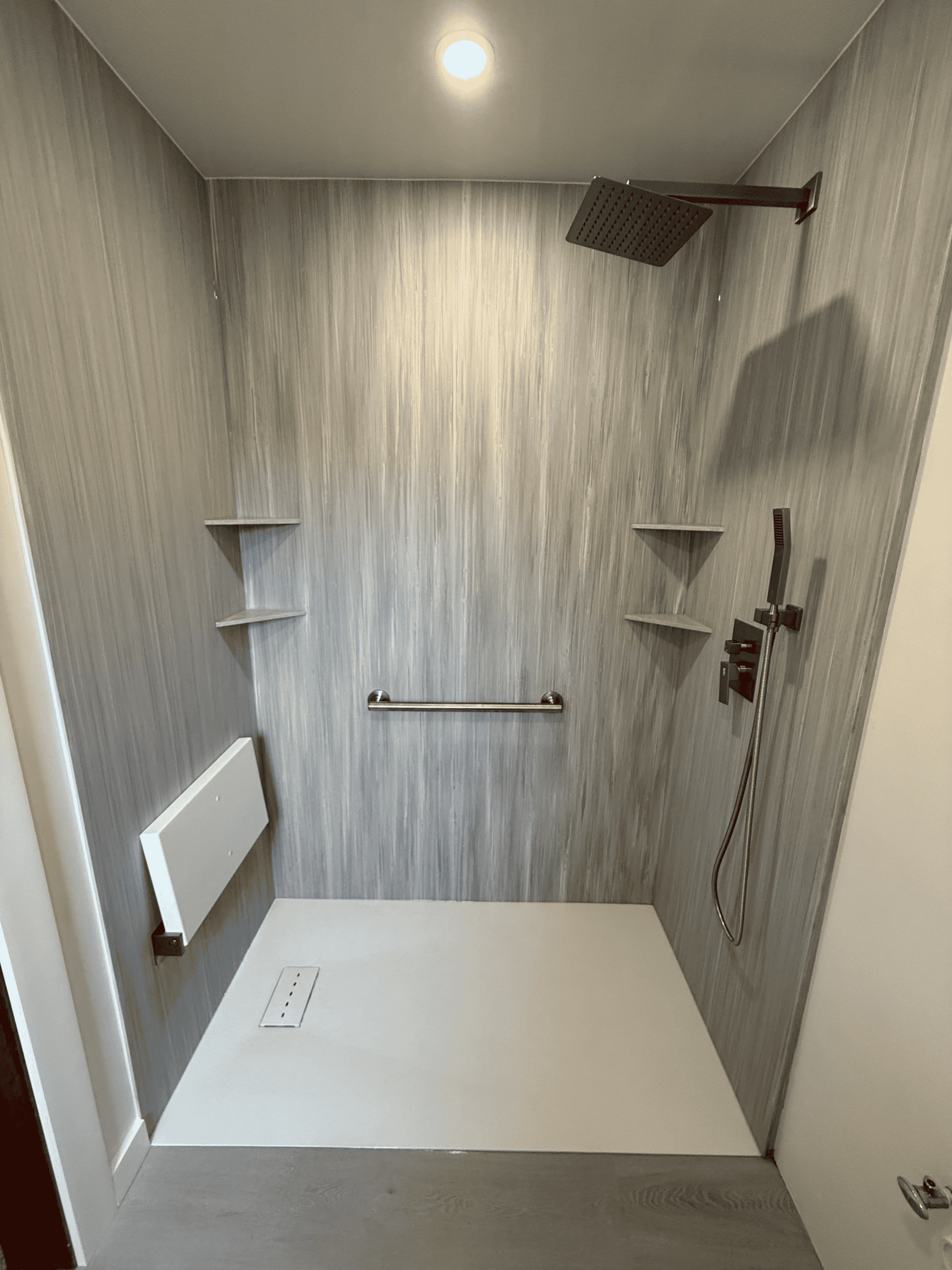 Modern walk-in shower with rainfall showerhead and safety grab bar in a stylish bathroom.