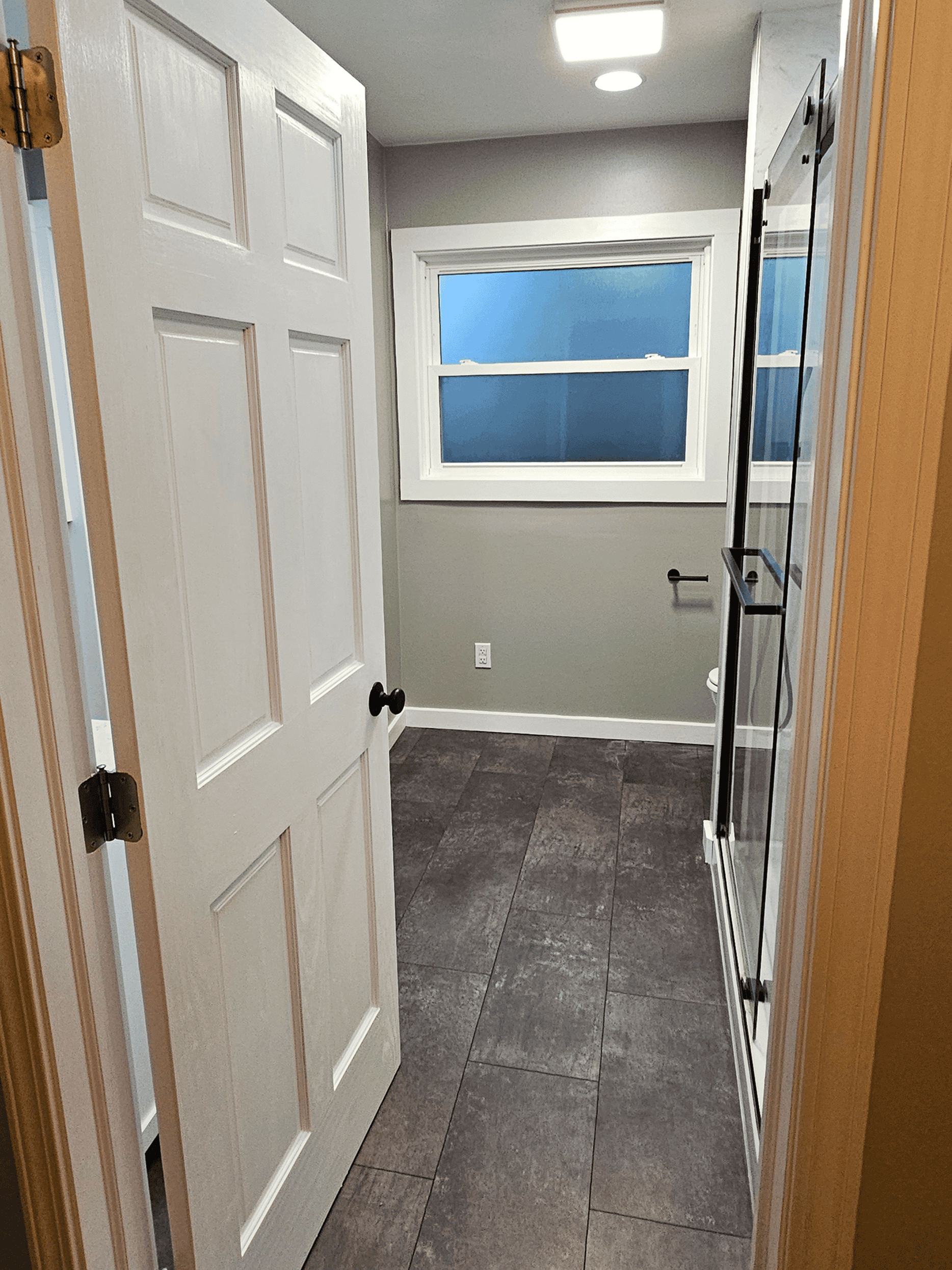 Modern bathroom with gray tile flooring, white walls, and a large window for natural light.