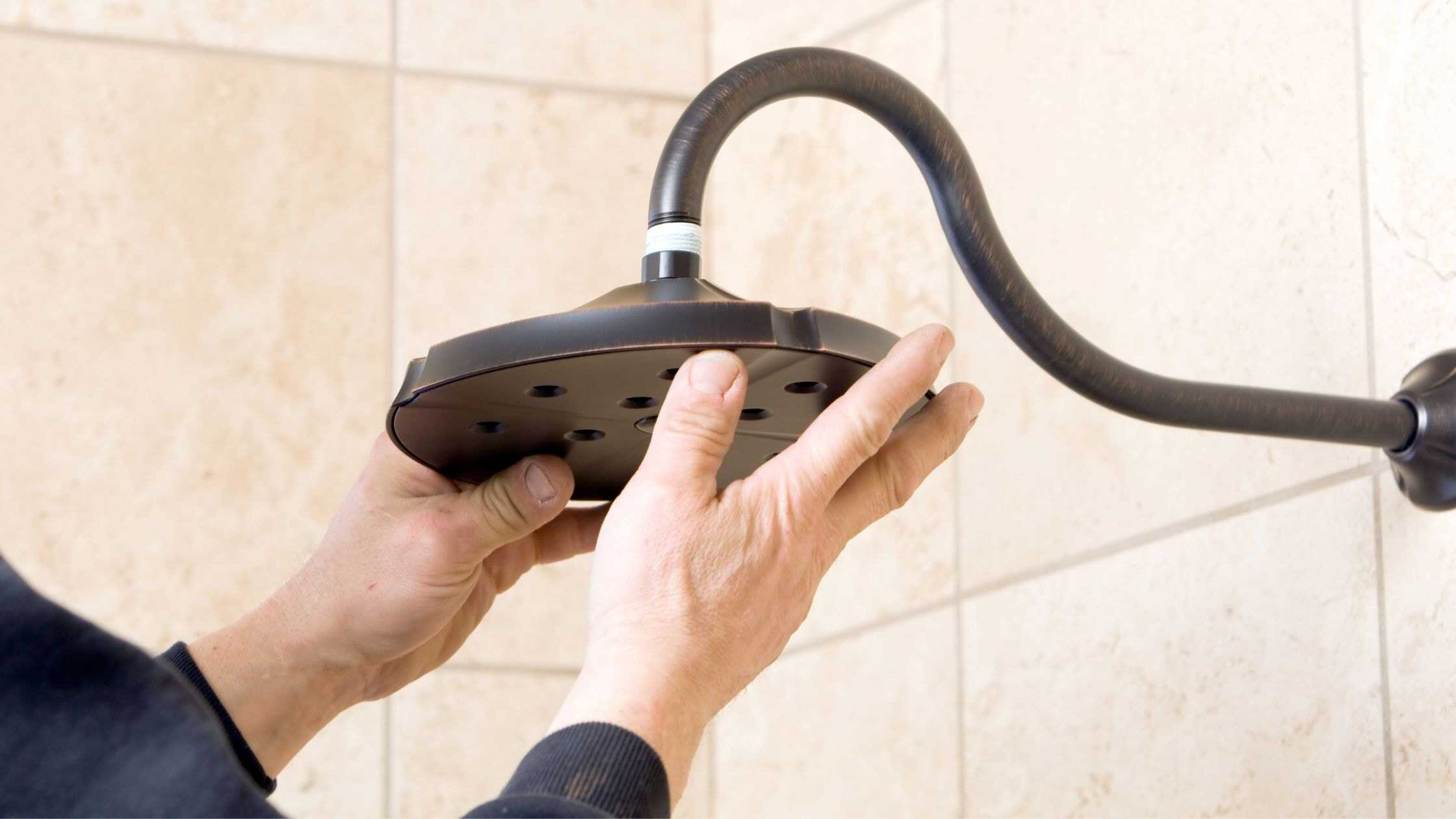 Hand installing a modern showerhead on a tiled bathroom wall.