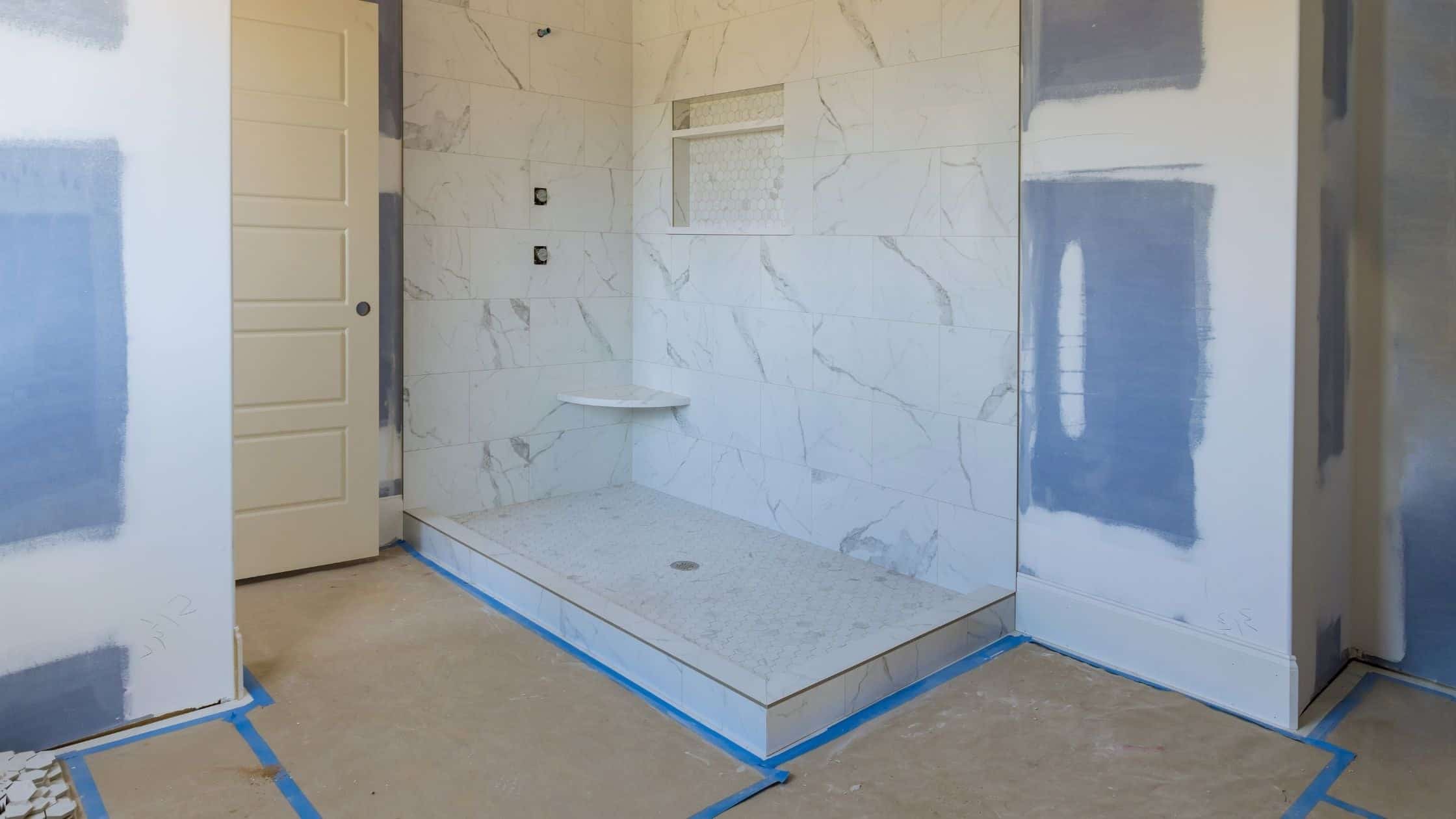 Modern shower area with white marble tiles and built-in bench in bathroom renovation.