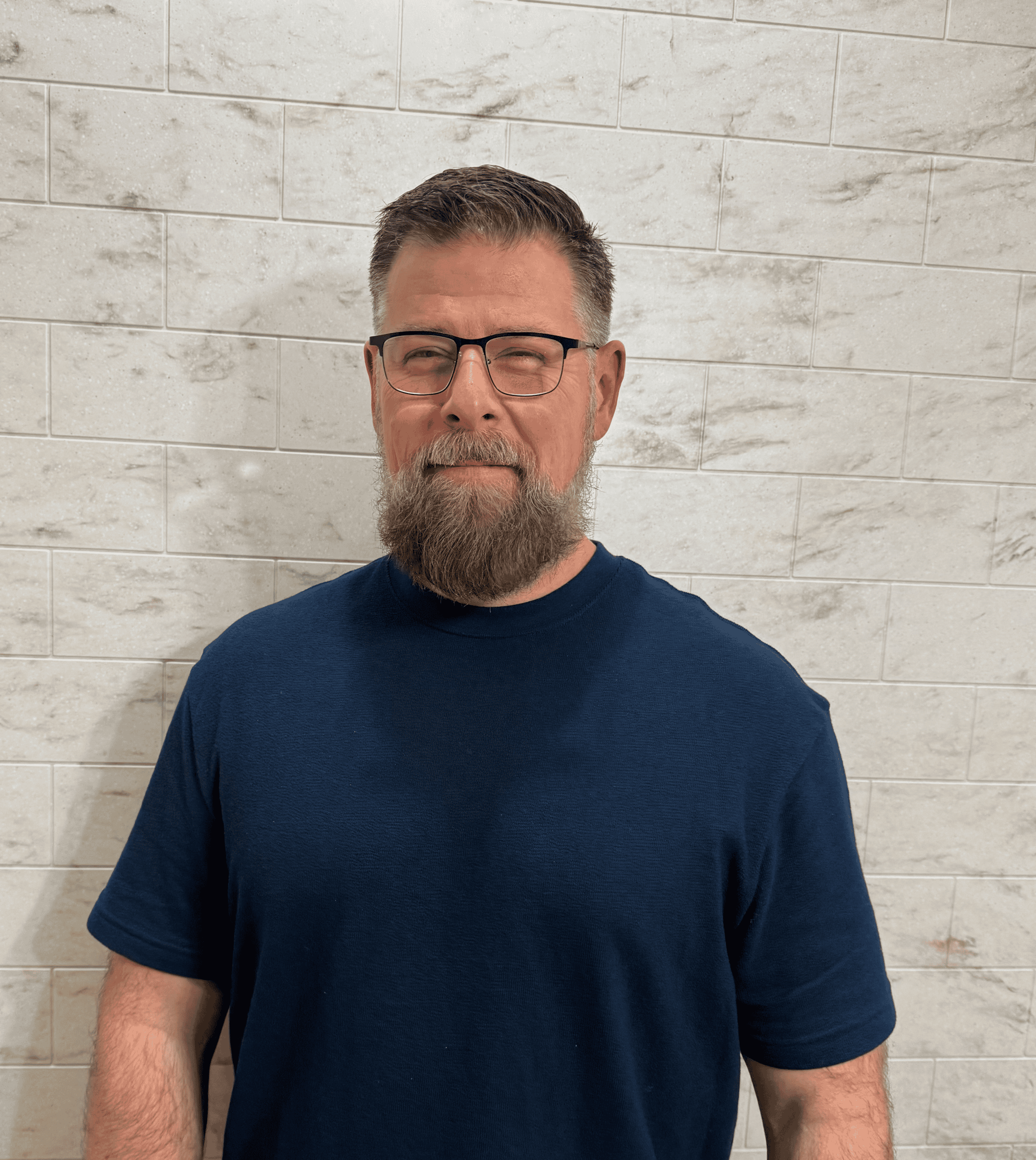 Man with glasses and beard standing against a white tiled wall, representing bathroom renovation ser.