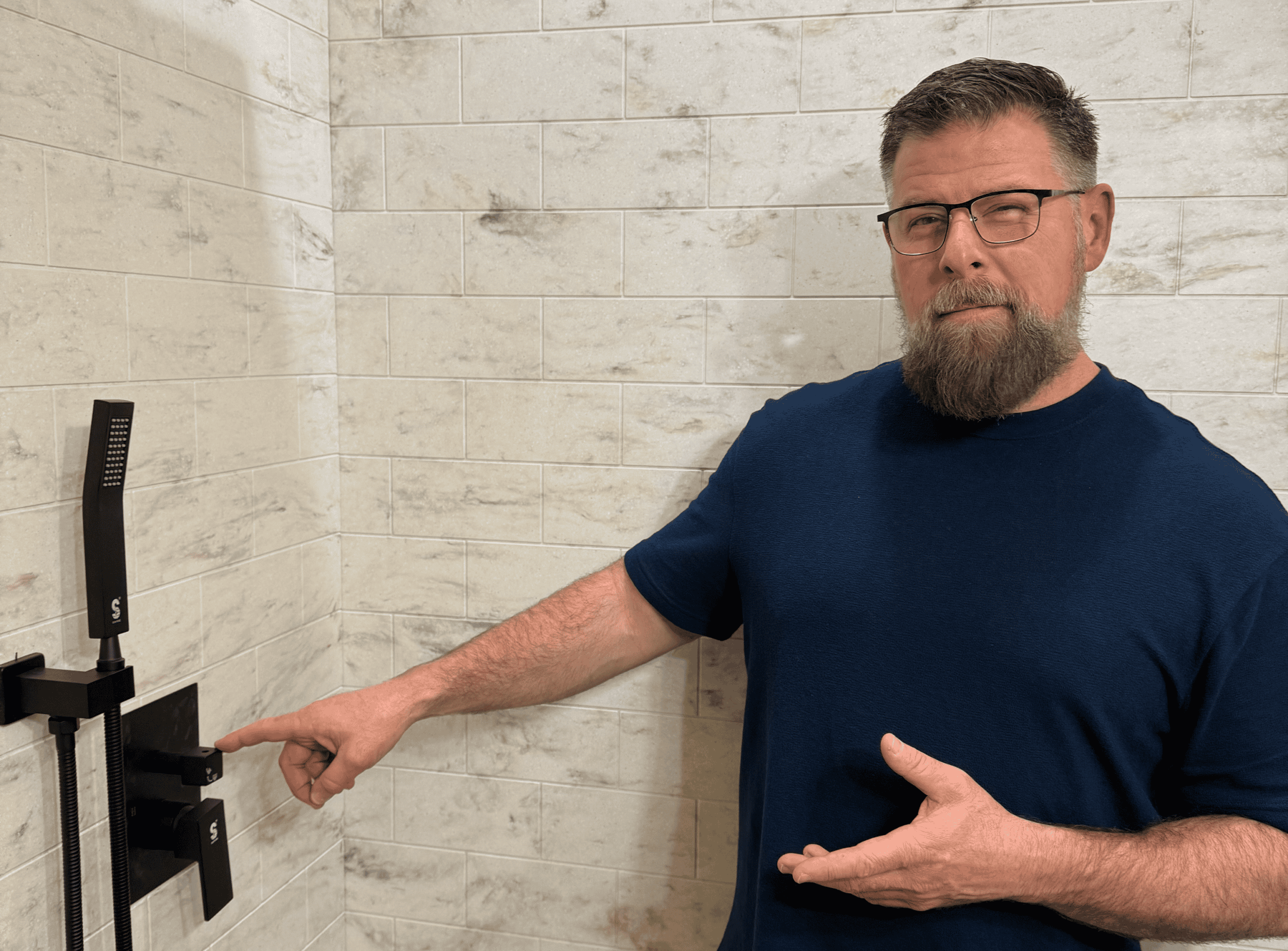 Man pointing at bathroom wall with shower fixtures, promoting bathroom renovation services.