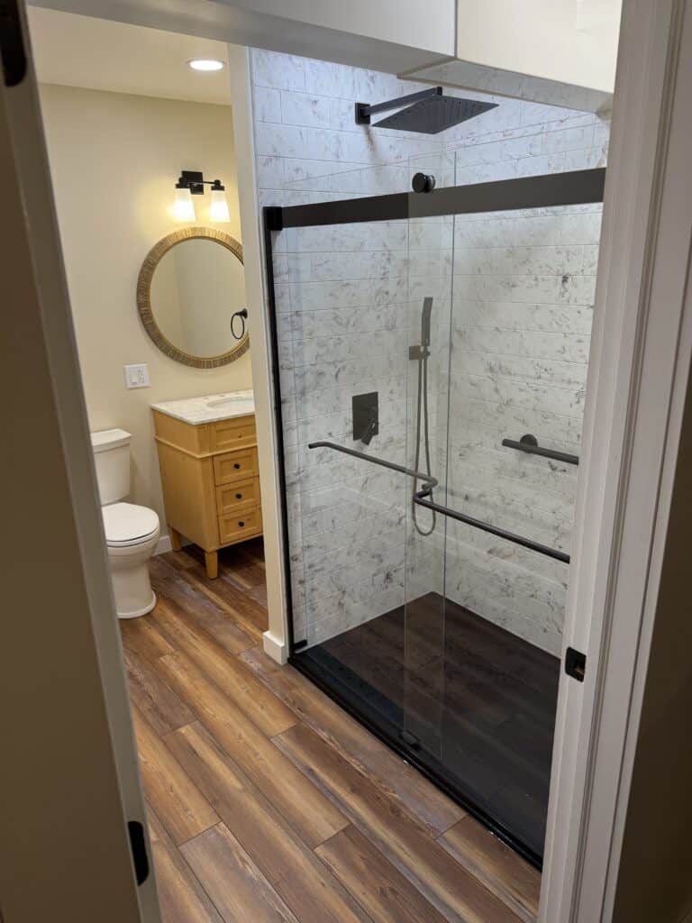 Stylish walk-in shower with glass enclosure, rainfall showerhead, and wood-look flooring.