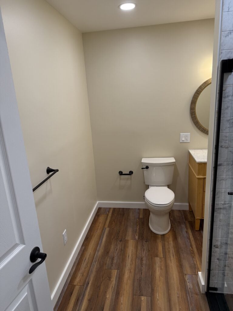 Toilet in a modern bathroom with beige walls and wooden flooring.