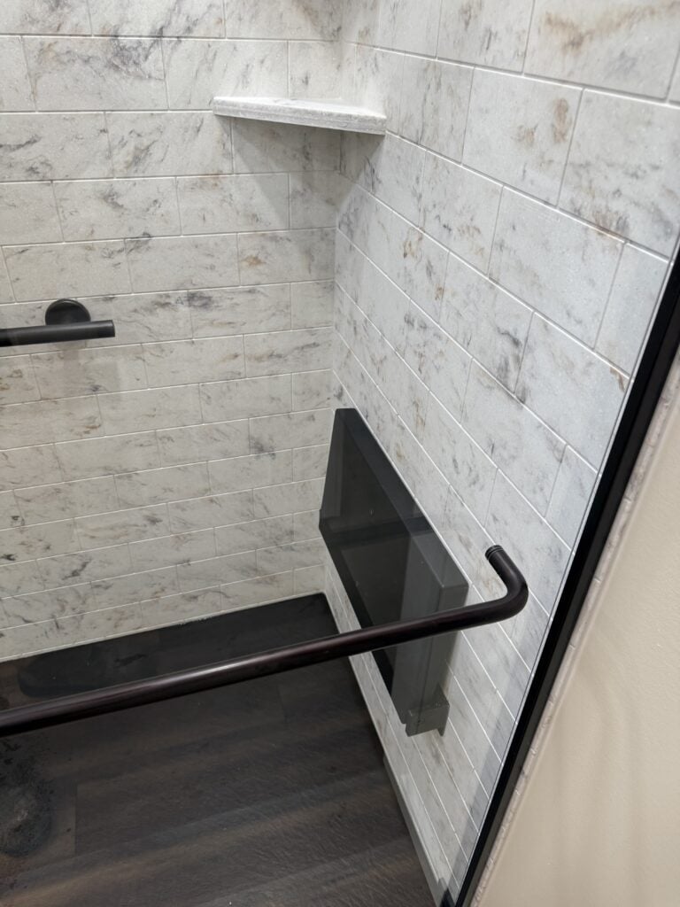 Modern shower wall with white marble-look tiles and black accents.