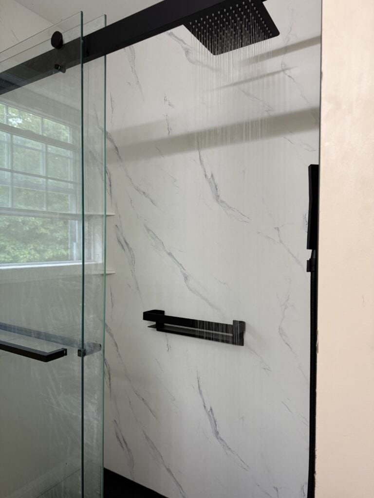 Modern marble shower wall with black fixtures and glass enclosure.