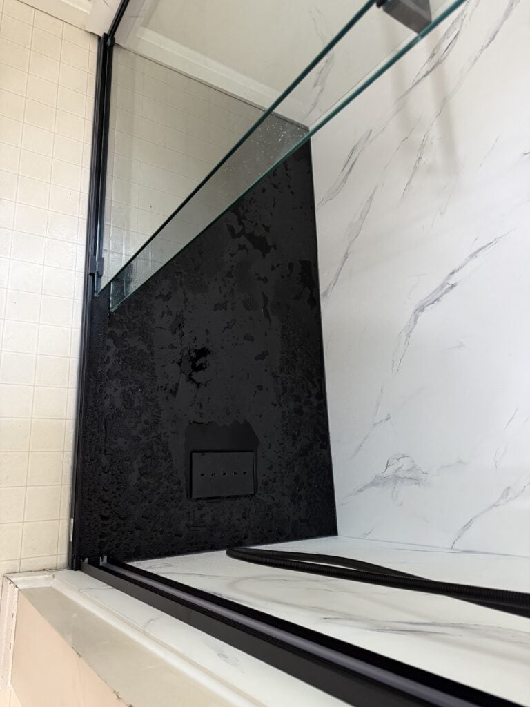 Modern shower wall with black and white marble tiles and glass partition.