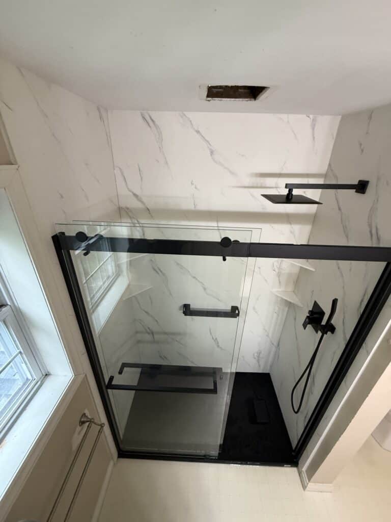 Modern glass shower with black fixtures and marble walls.