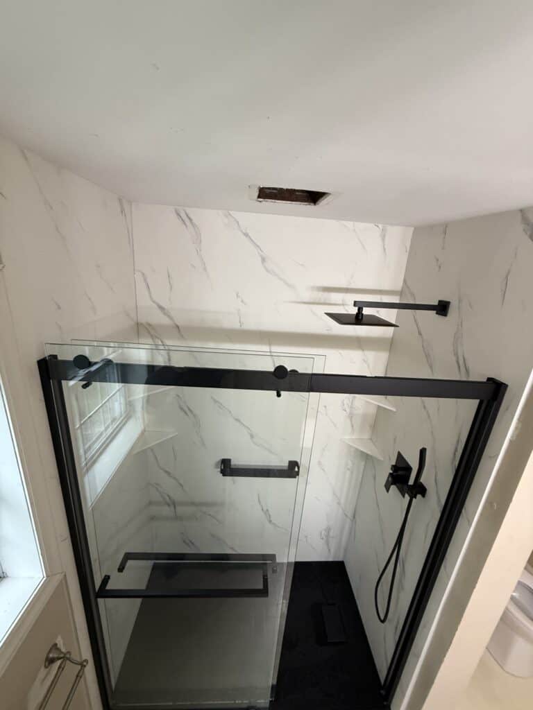 Modern walk-in shower with glass enclosure and marble walls.