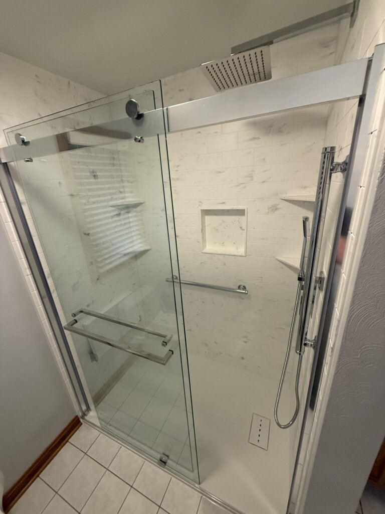 Accessible walk-in shower with glass doors and built-in shelves.