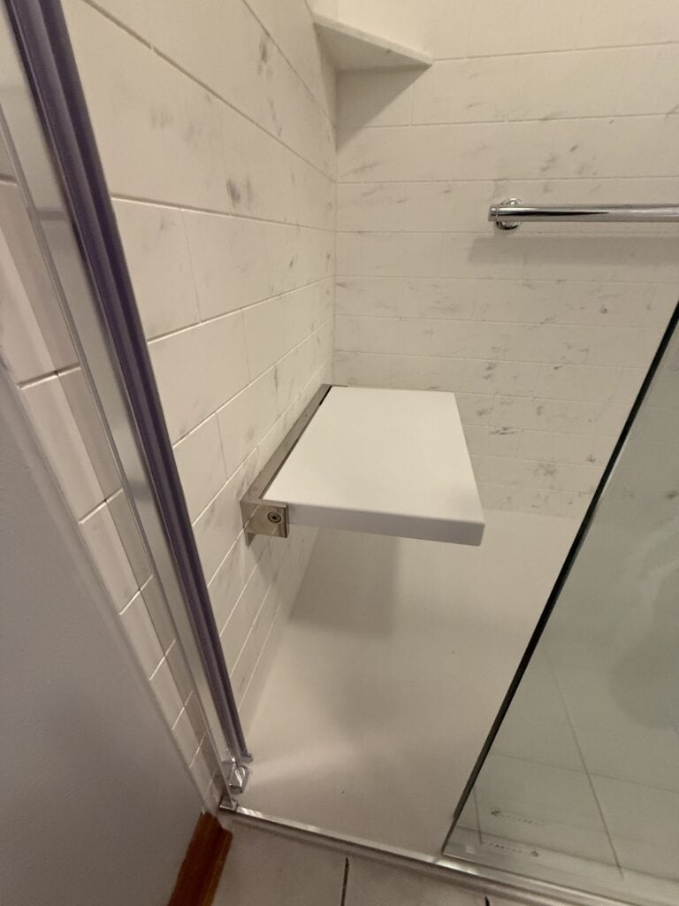 Shower bench installed in a modern bathroom with white marble walls for comfort and convenience.