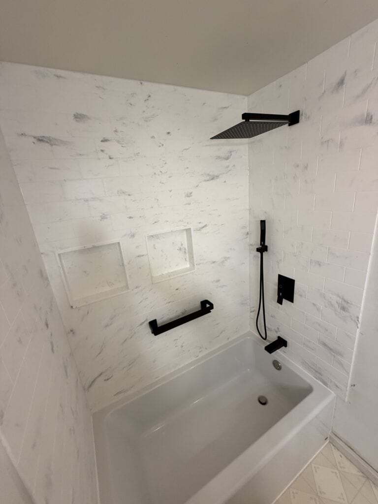 Modern shower with black fixtures, rain showerhead, and built-in niches in a white tiled bathroom.