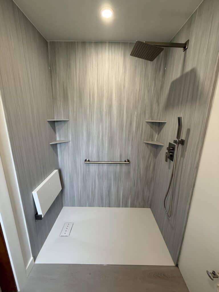 Modern walk-in shower with gray wall panels and built-in corner shelves.