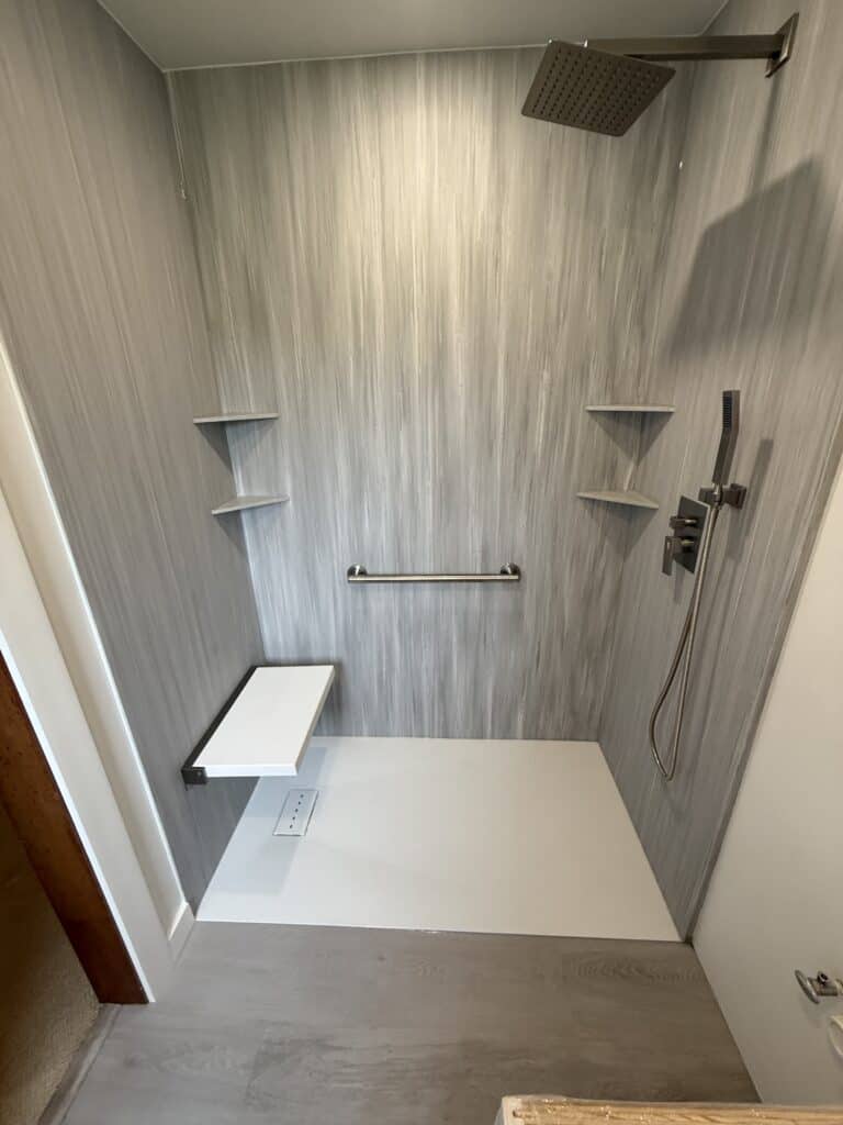 Modern walk-in shower with sleek gray wall panels and built-in shelves.