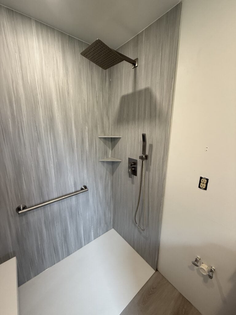 Shower with rainfall head, handheld sprayer, and safety grab bar in a contemporary bathroom.