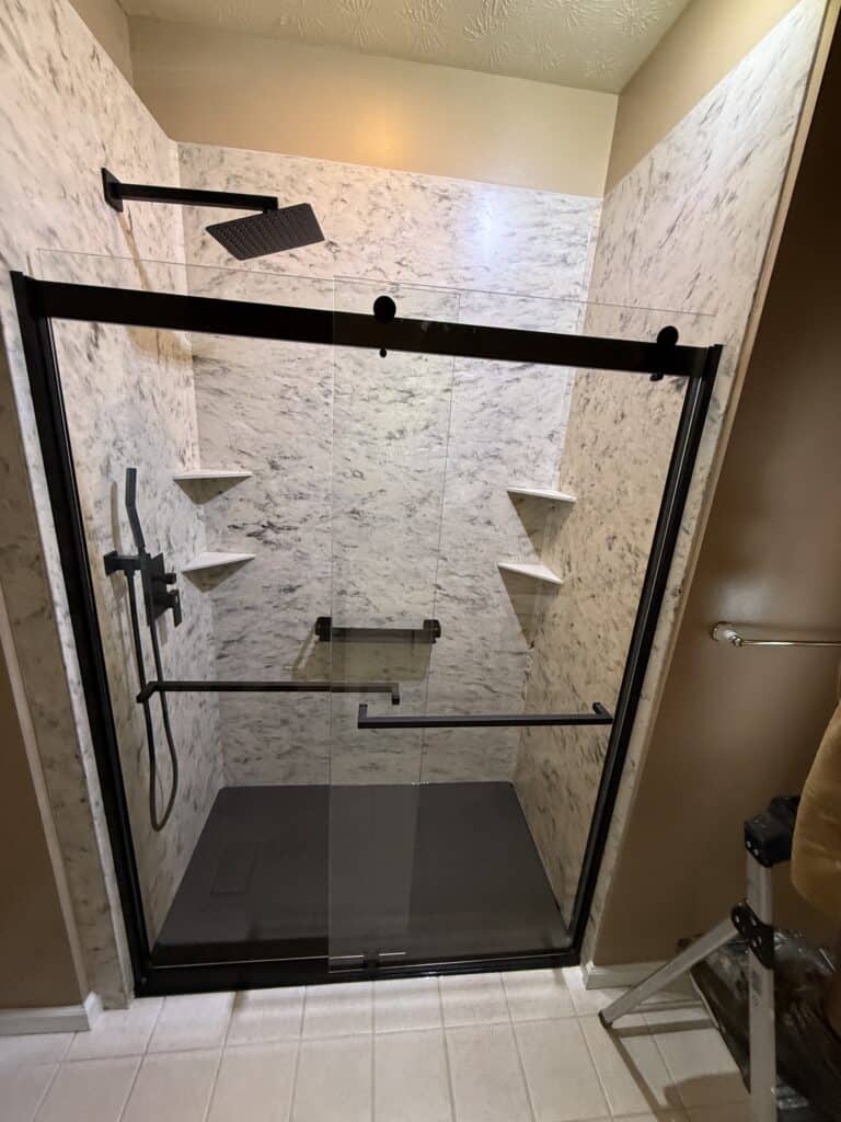 Shower enclosure with black frame, marble walls, and built-in corner shelves.