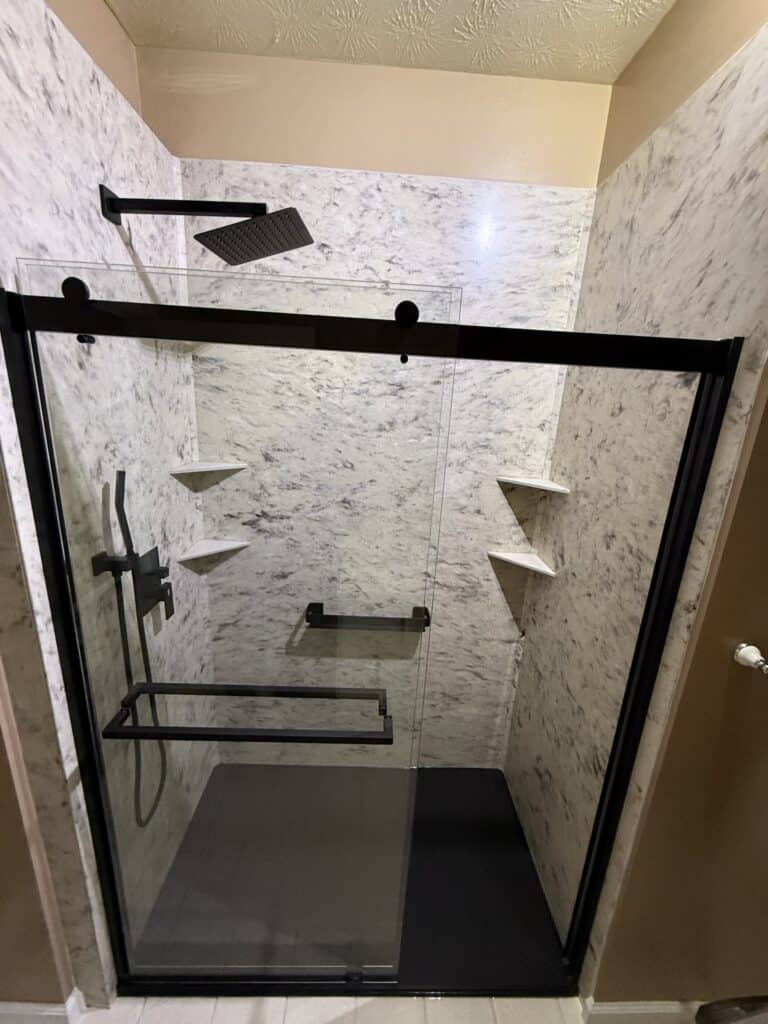 Elegant walk-in shower with black fixtures and marble walls.
