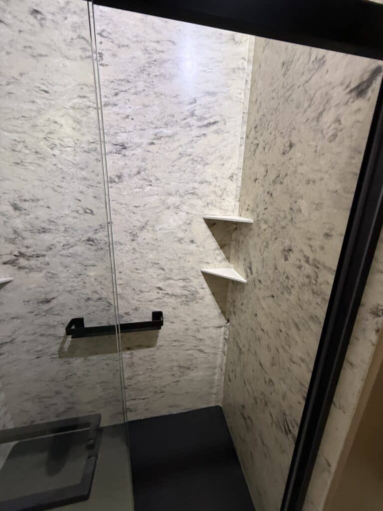 Shower niche with two shelves in a modern bathroom, featuring marble walls and a glass door.