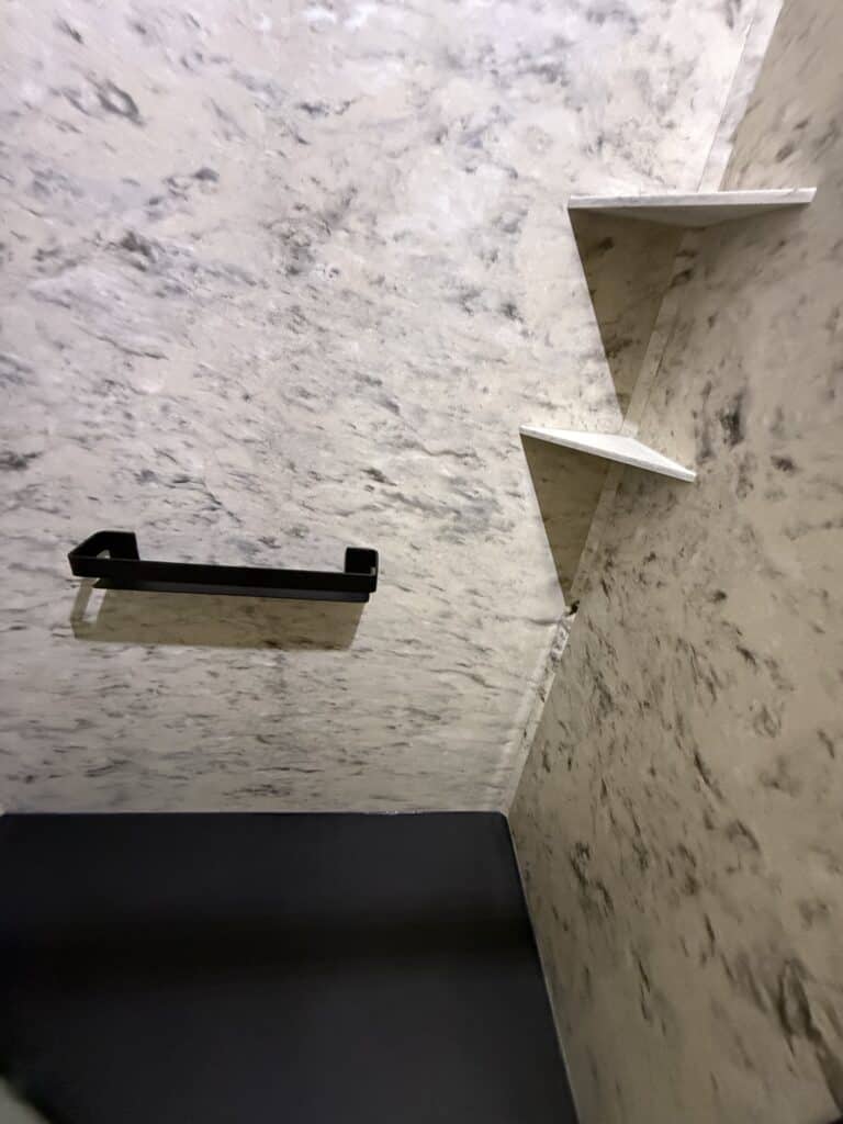 Modern shower niche with two white shelves on a textured marble wall.