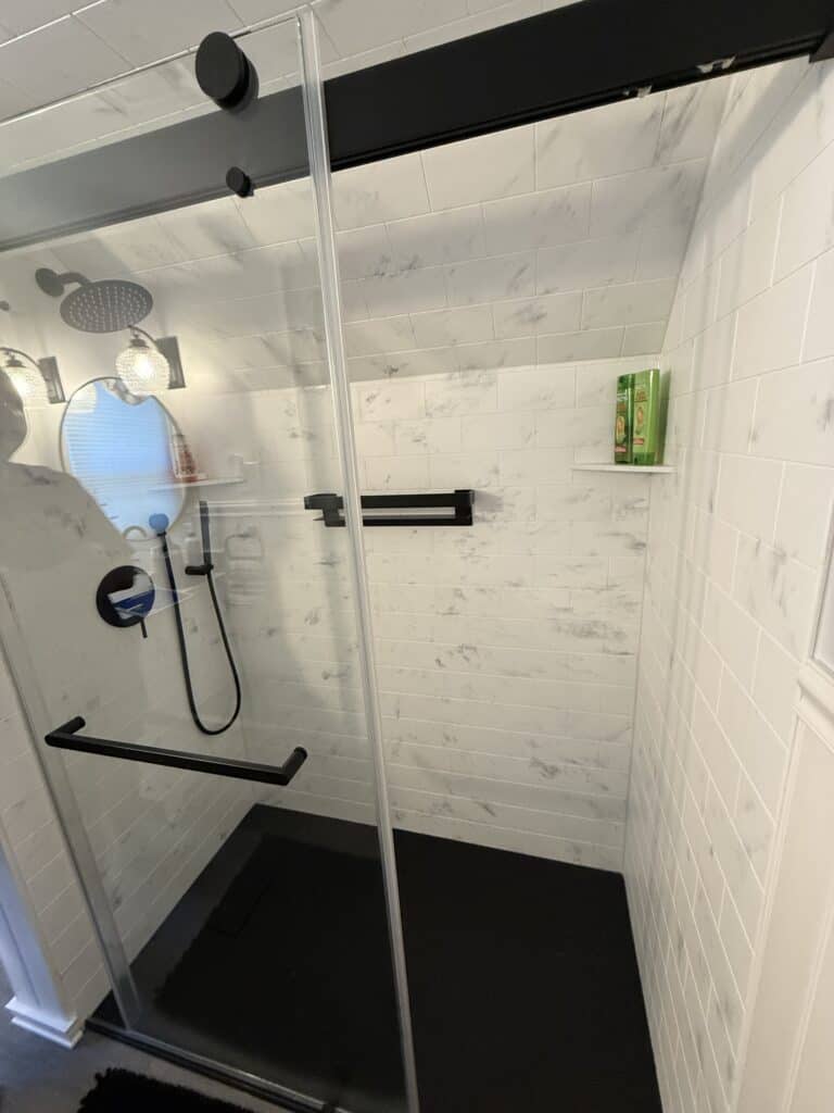 Shower with black fixtures and white tiled walls, featuring a glass door and a built-in shelf for to.