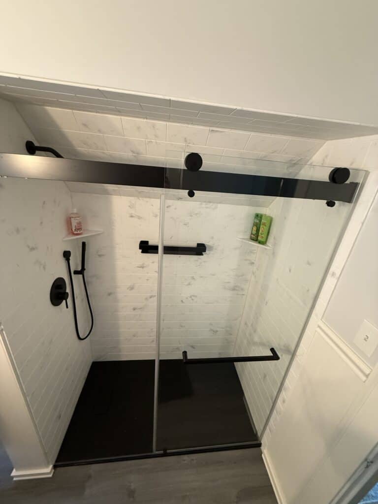 Stylish glass shower with black fixtures and white tiled walls.