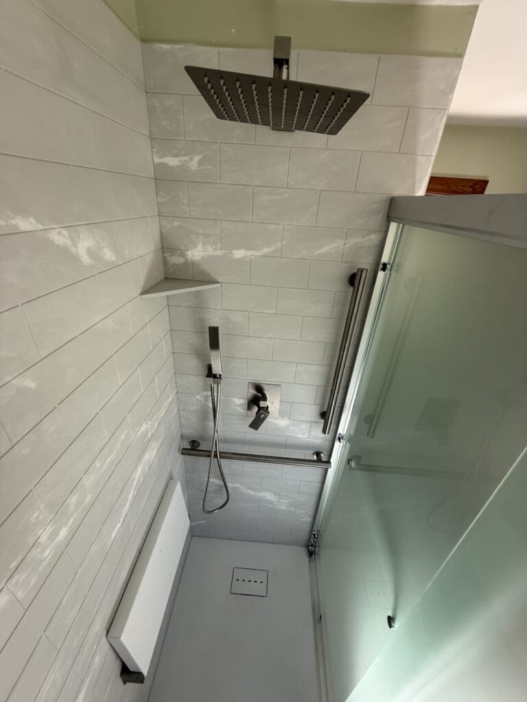 Modern shower with rainfall head, handheld shower, and glass enclosure in a sleek bathroom.