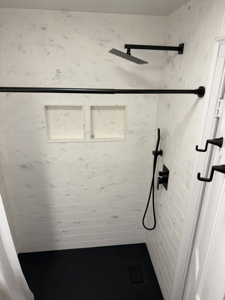 Modern shower with black fixtures, rainfall showerhead, and white tiled walls.