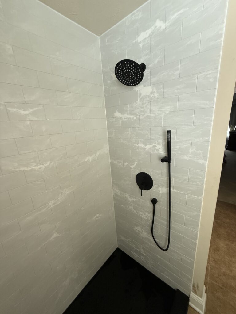 Modern shower with black rainfall head and handheld sprayer in a sleek tiled bathroom.