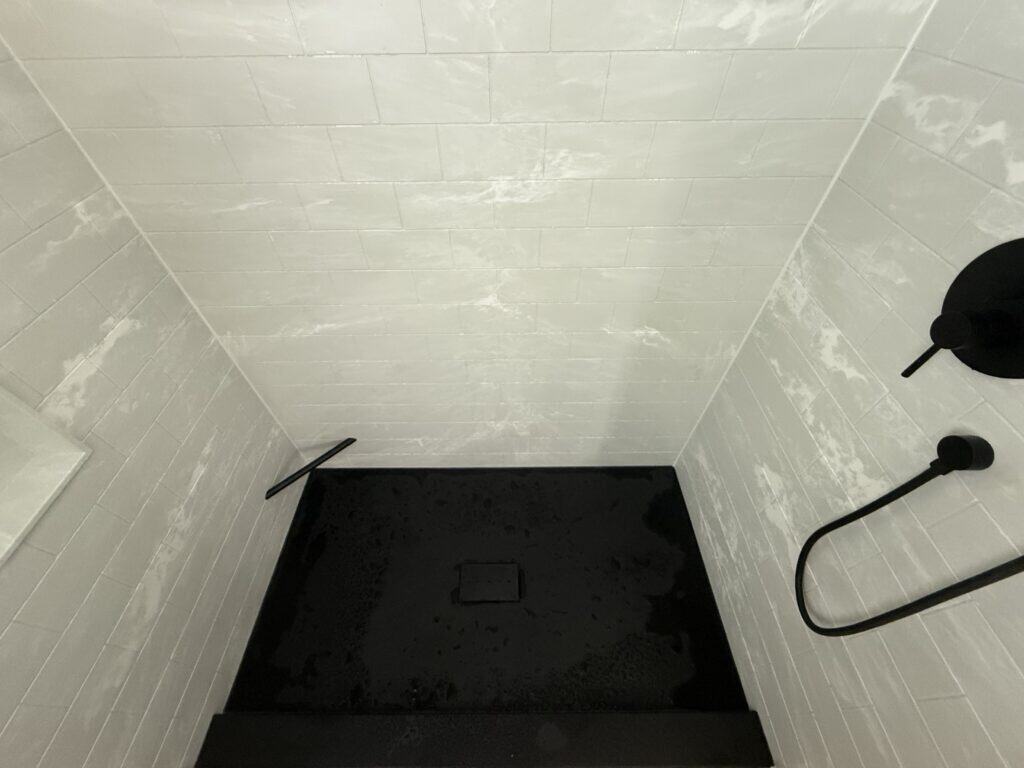 Modern walk-in shower with sleek black fixtures and white tile walls.