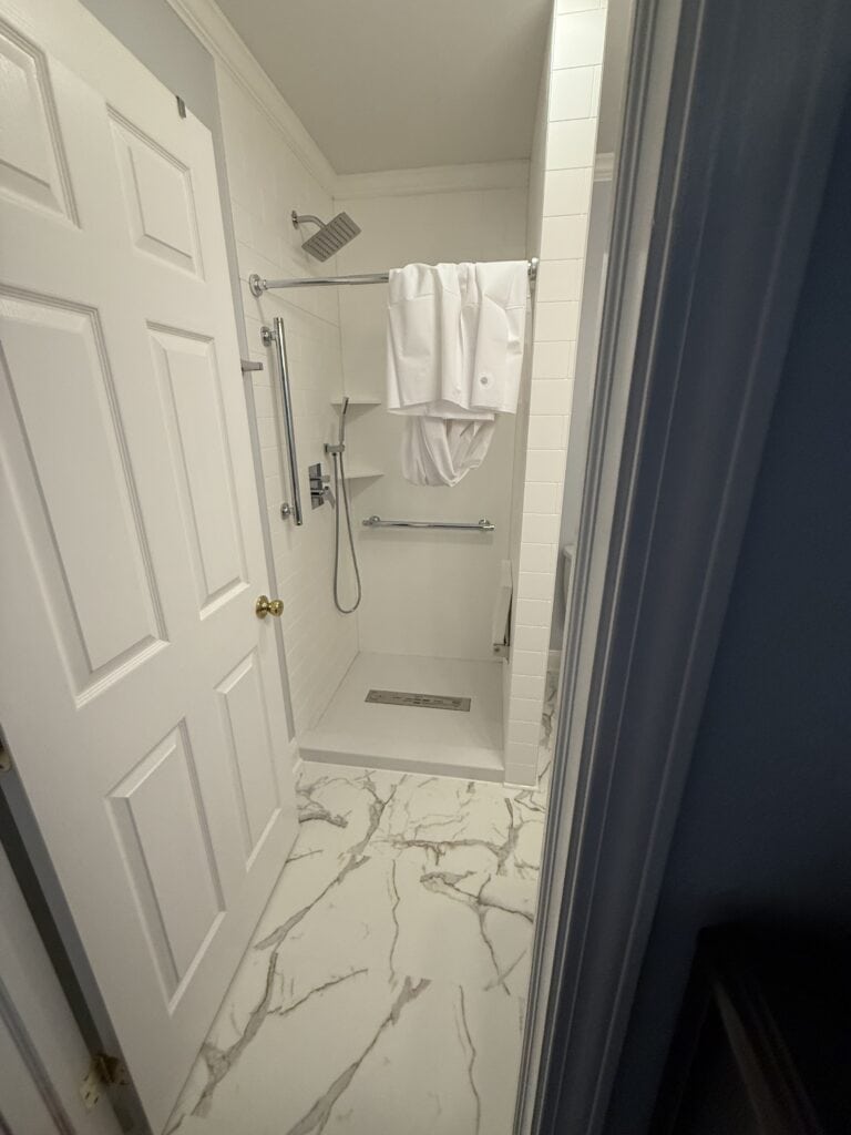 Modern walk-in shower with white tiles, rainfall showerhead, and towel rack.