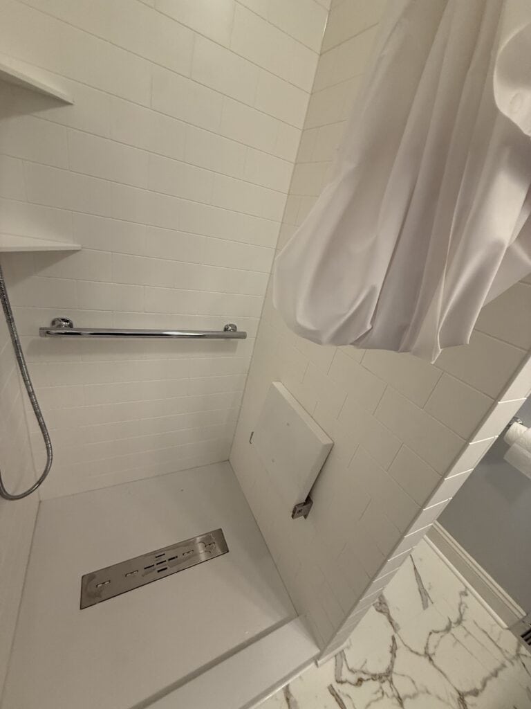 Shower with white curtain and wall-mounted shelves in a modern bathroom.