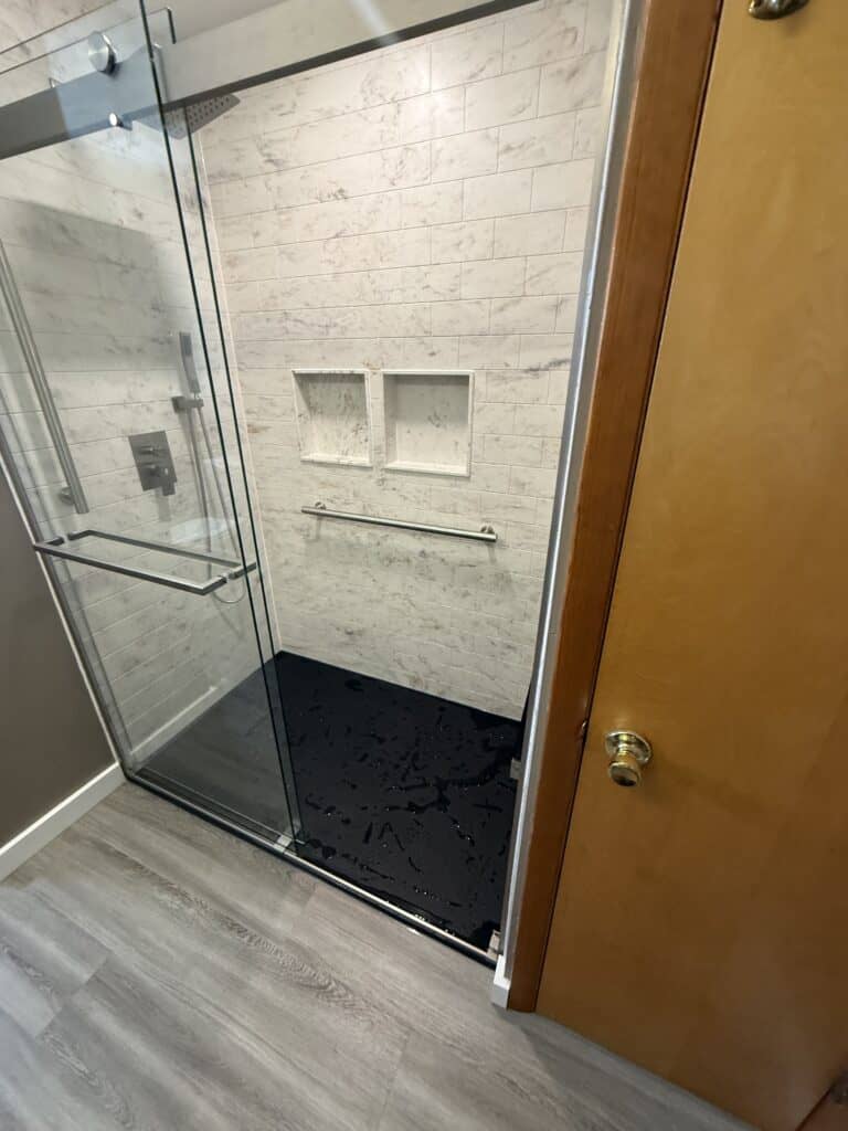 Shower with glass door and built-in niches for toiletries. Elegant bathroom design with white tiles.