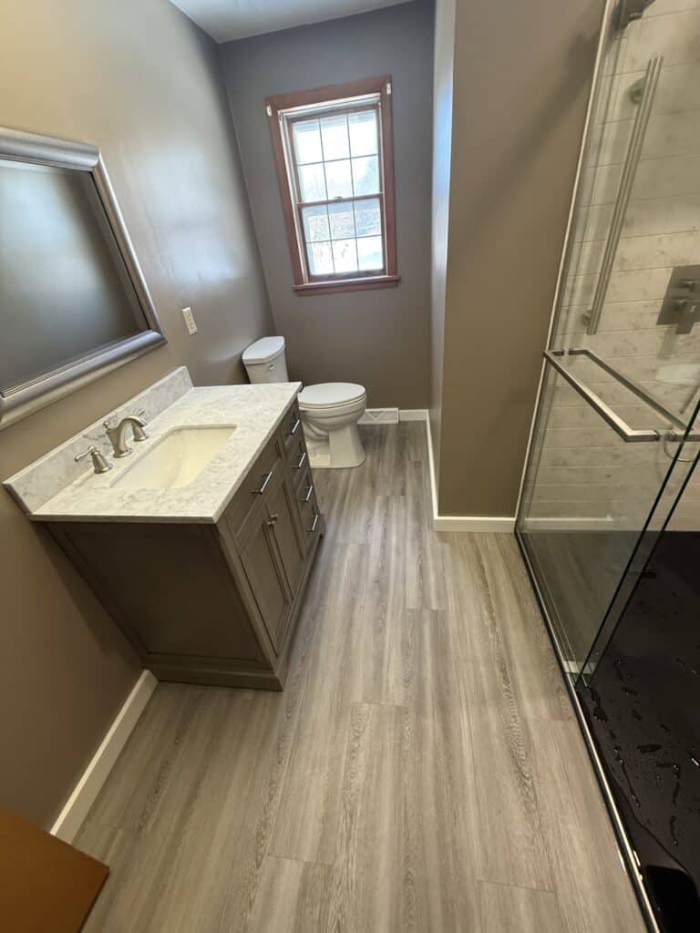 Modern bathroom with gray vanity, large mirror, and glass shower enclosure.