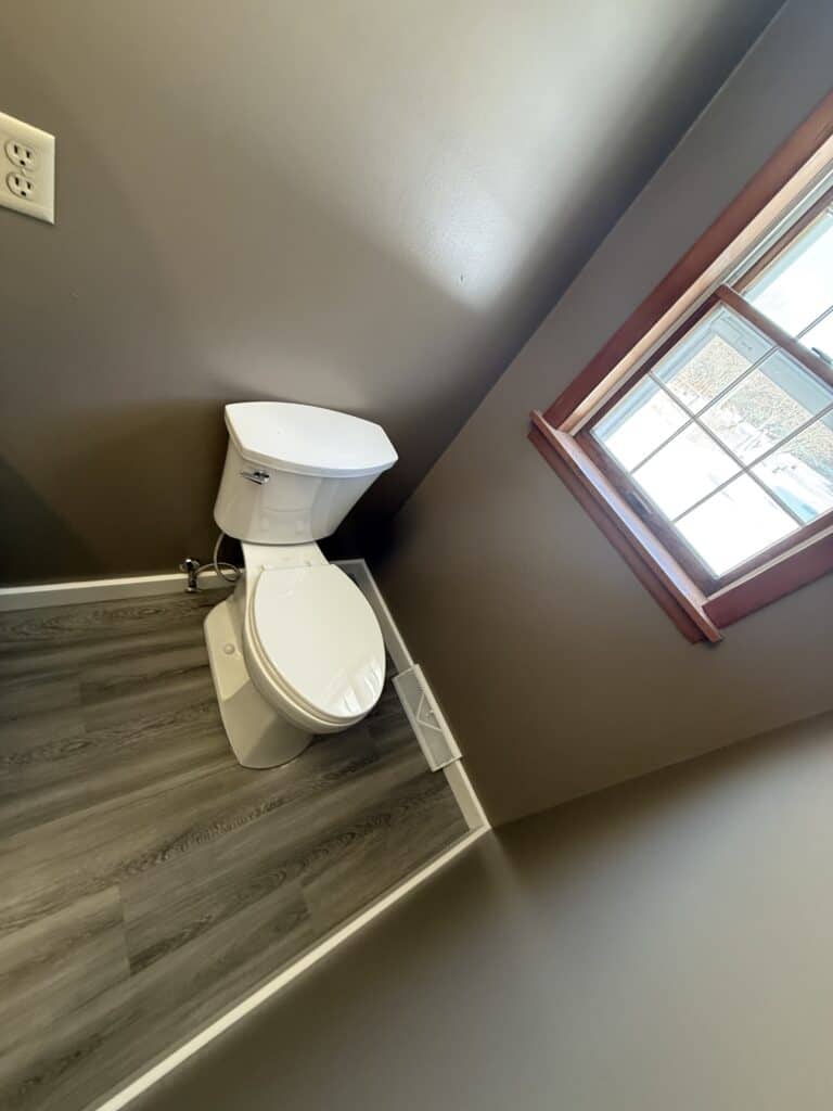Toilet installed in a small, modern bathroom with gray walls and a wooden window frame.