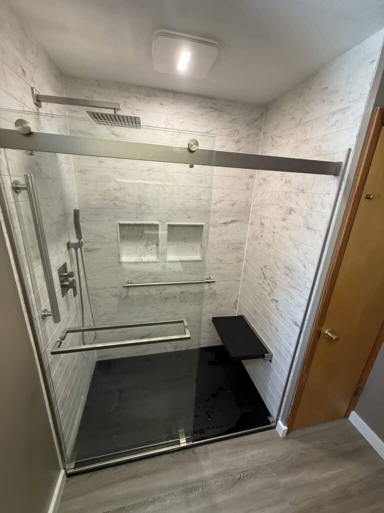 Enclosed walk-in shower with glass doors, rainfall showerhead, and built-in niche for toiletries.