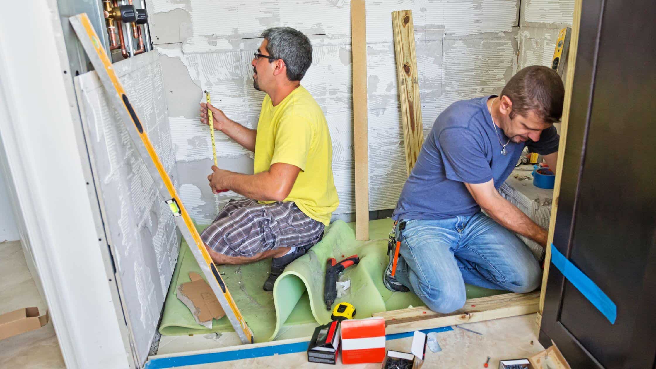 Two workers installing tiles in a bathroom renovation project.