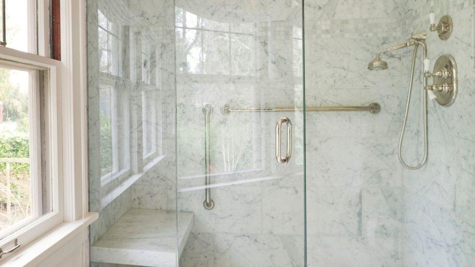 Modern marble shower with accessible grab bars and glass enclosure in a luxurious bathroom.