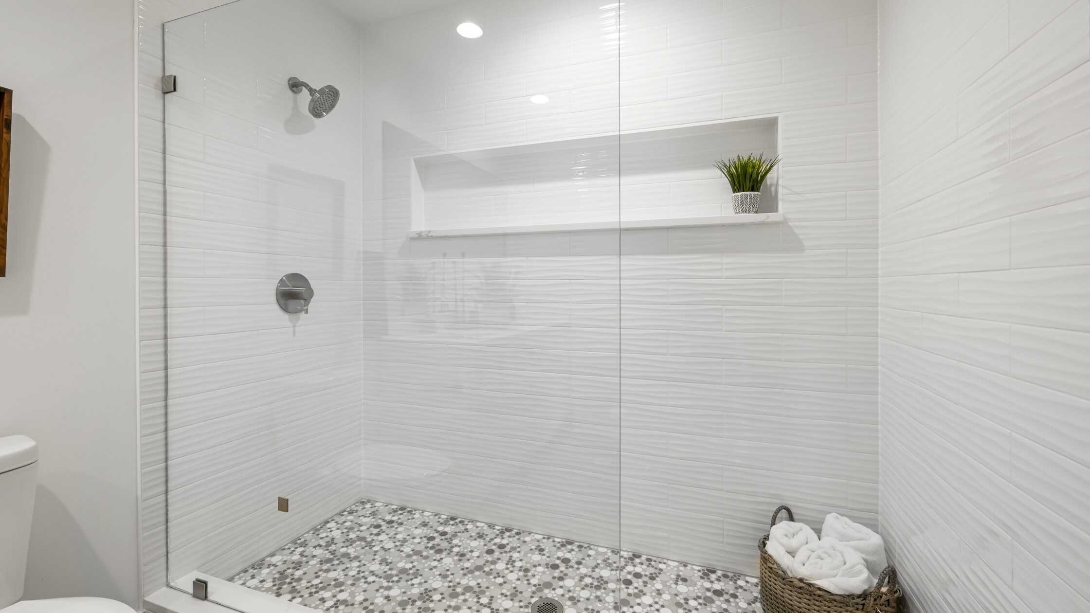 Bright modern shower with white tiles, built-in shelf, and pebble floor in a bathroom.