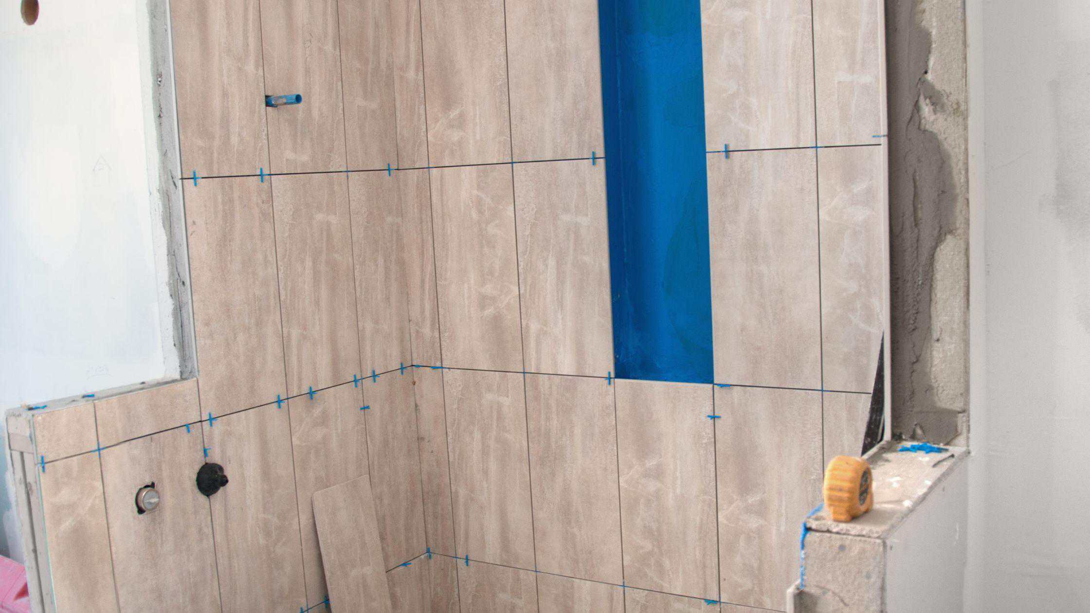 New bathroom wall tiles installation with beige and blue tiles in progress.