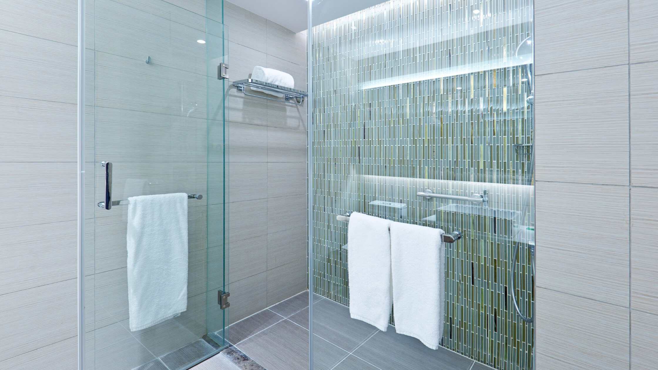 Modern glass shower with green mosaic tiles and accessible grab bars in a contemporary bathroom.